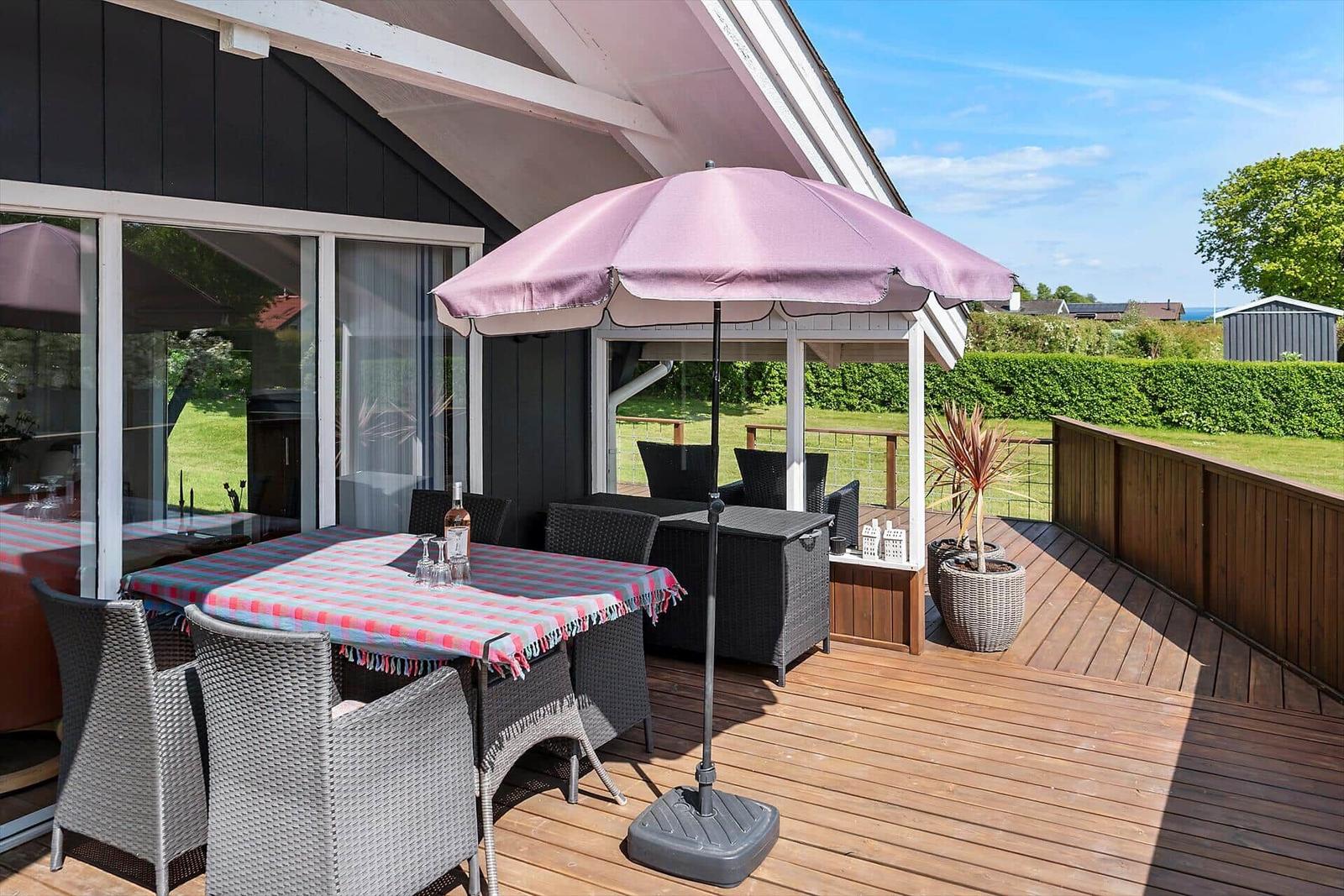 Terrasse mit Tisch, Stühlen und Sonnenschirm. Holzdecke und Blick auf Grünfläche.