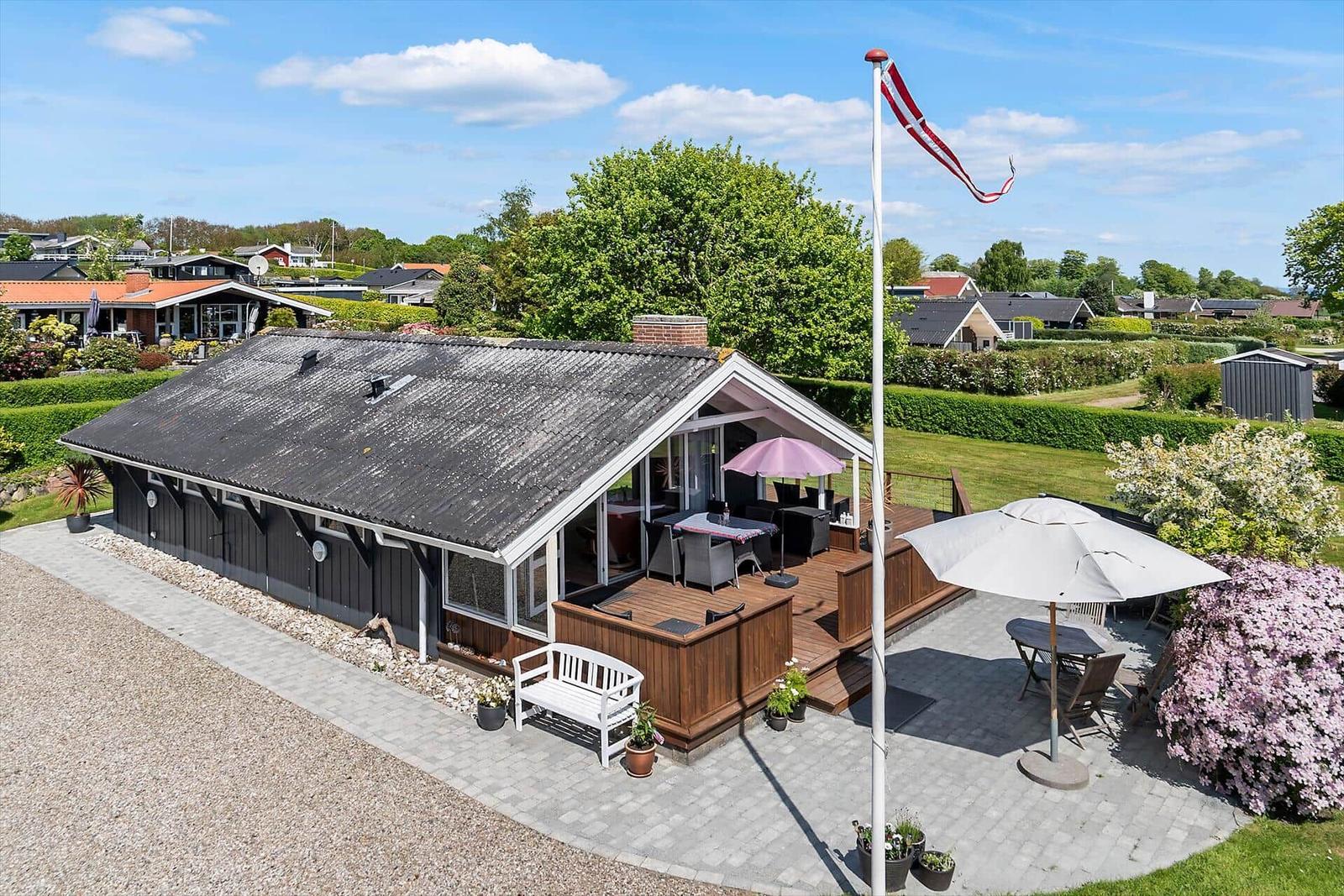 Haus mit Terrasse, Garten und Flagge. Möblierte Außenterrasse mit Sonnenschirmen.