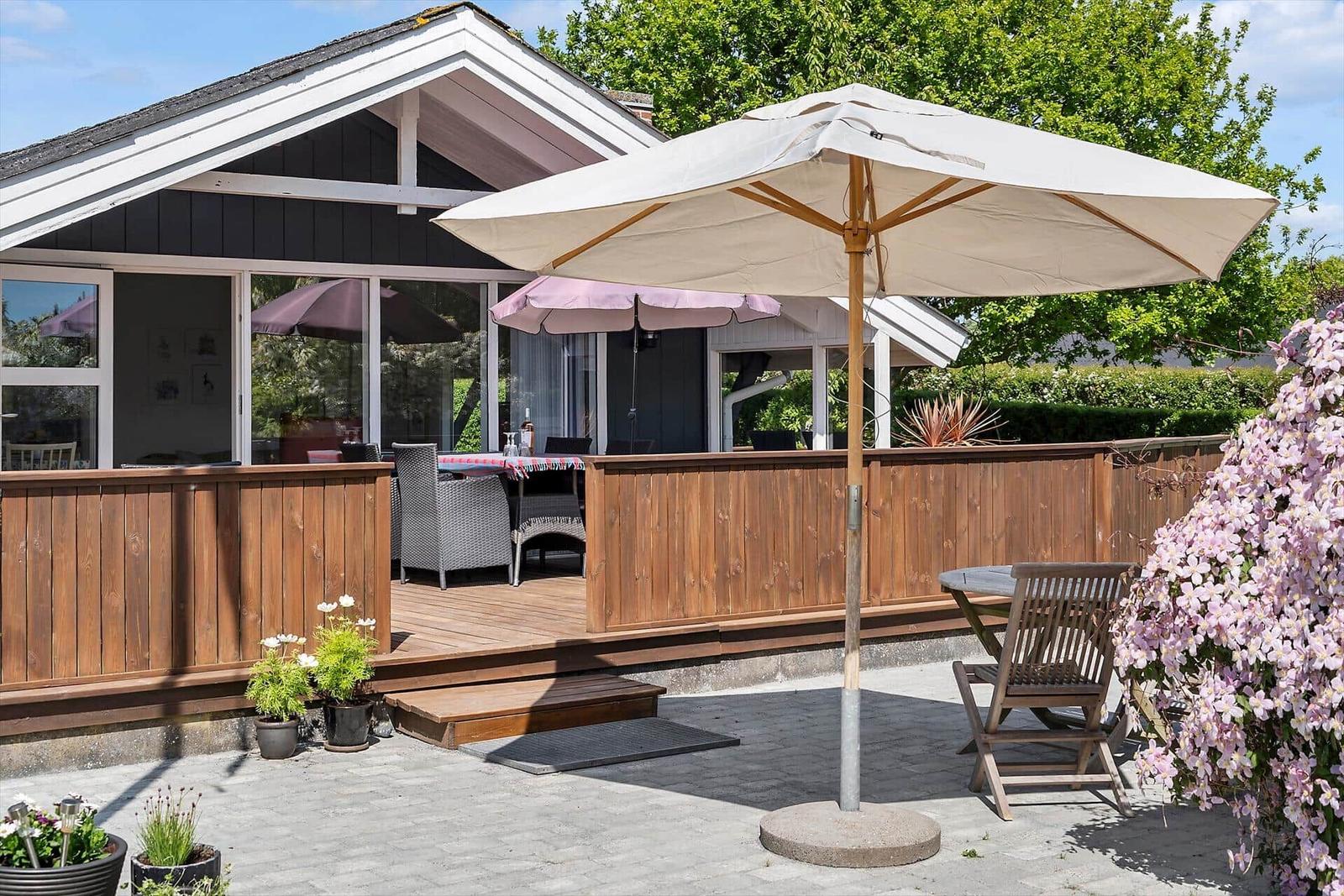 Terrasse mit Sonnenschirm und Tisch. Holzgeländer und Blumenbeete.