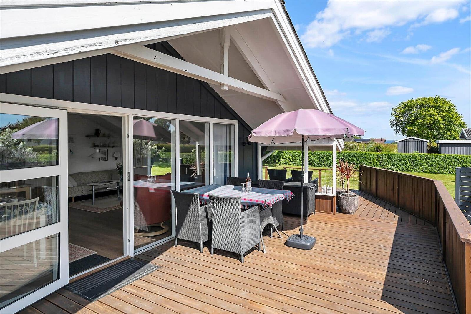 Terrasse mit Tisch, Stühlen und Sonnenschirm. Durchgehende Glasfront zur Wohnung.