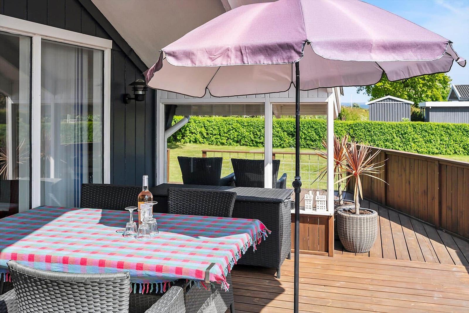 Terrasse mit Tisch, Stühlen und Sonnenschirm. Holzdecke, Pflanze und Blick auf Grün.