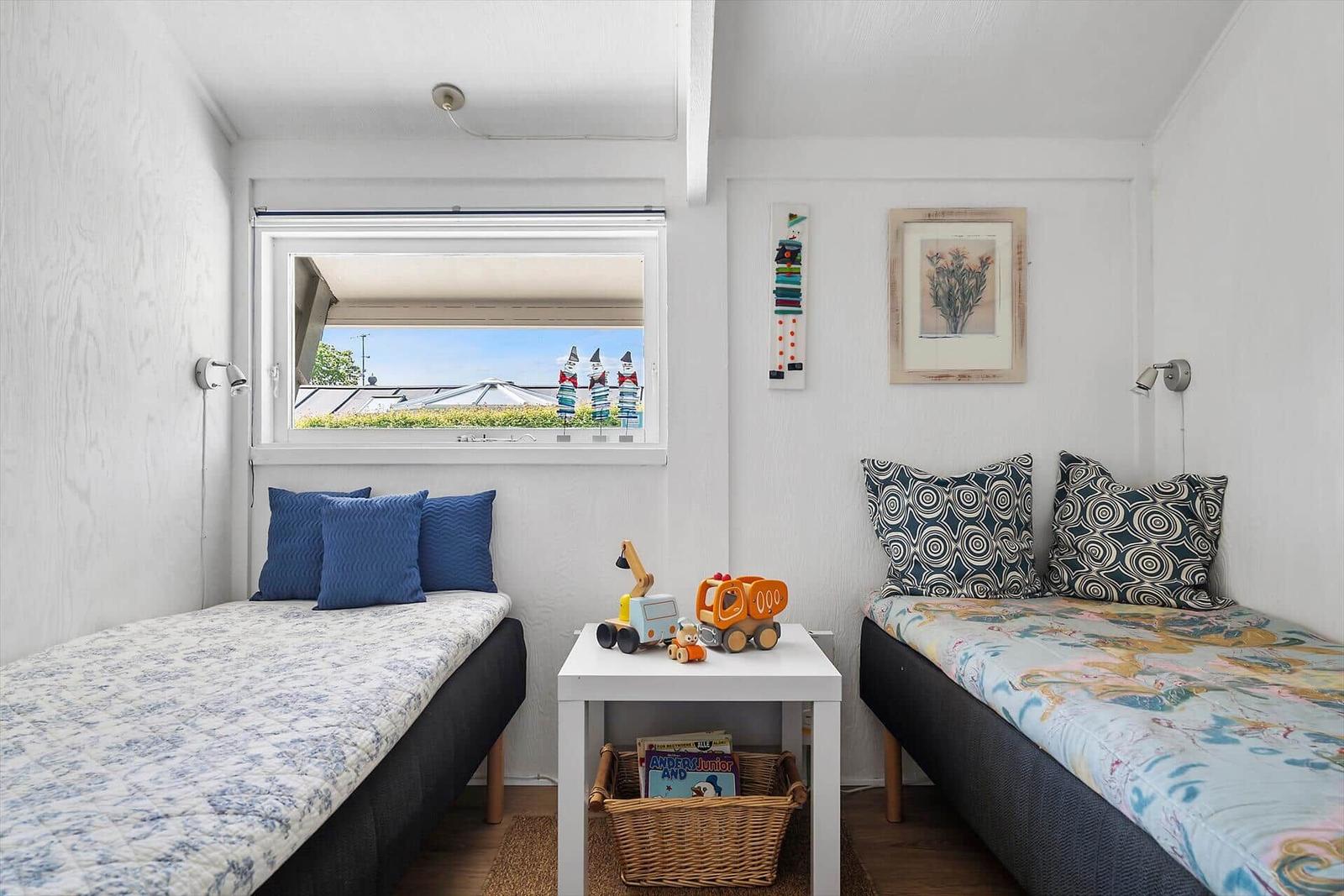 Zwei Betten mit Kissen und Spielzeug. Fenster mit Blick auf Dächer.