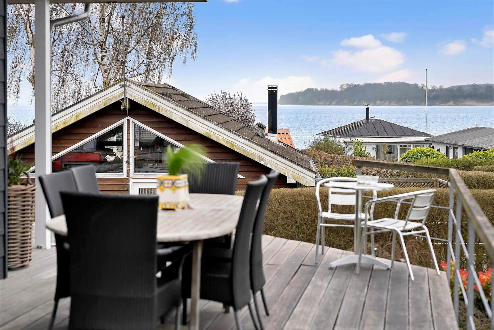 Deck with tables and chairs, view of water and houses.