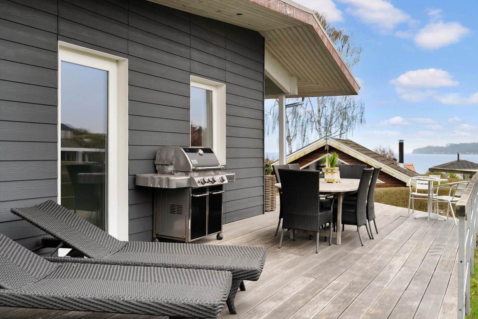 Deck with grill, loungers, and table. View of water and sky.
