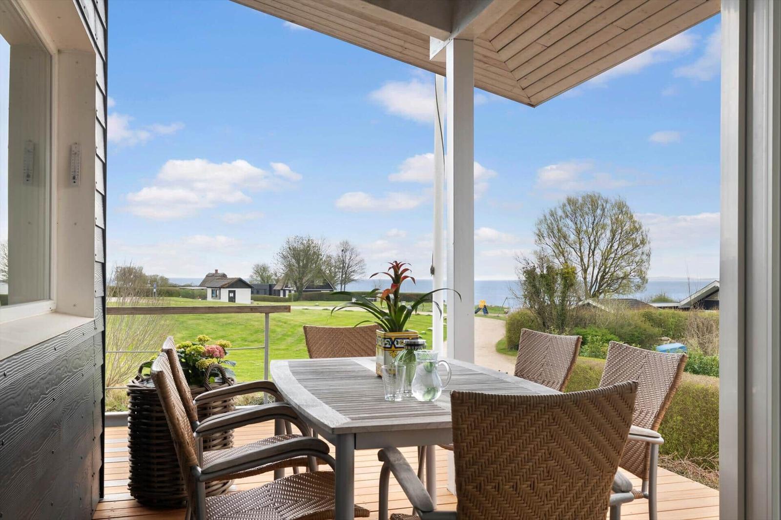 Terrace with table and chairs, view of grassland and sea.