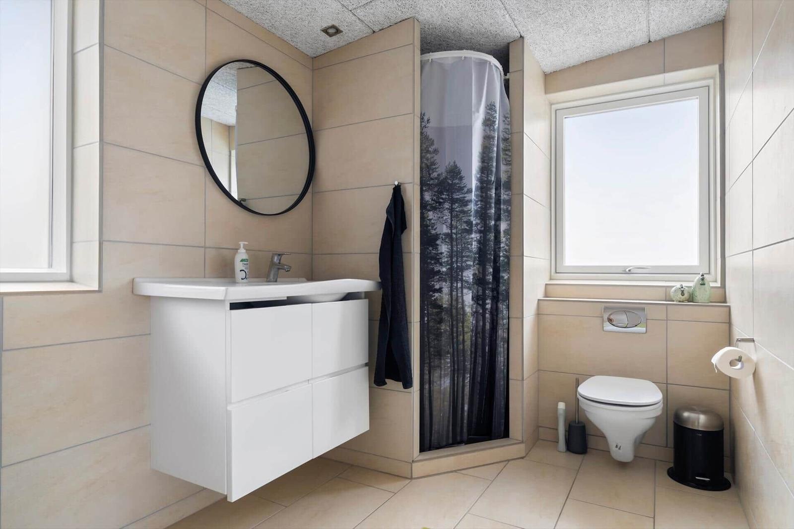 Bathroom with sink, shower, and toilet. Mirror and window visible.