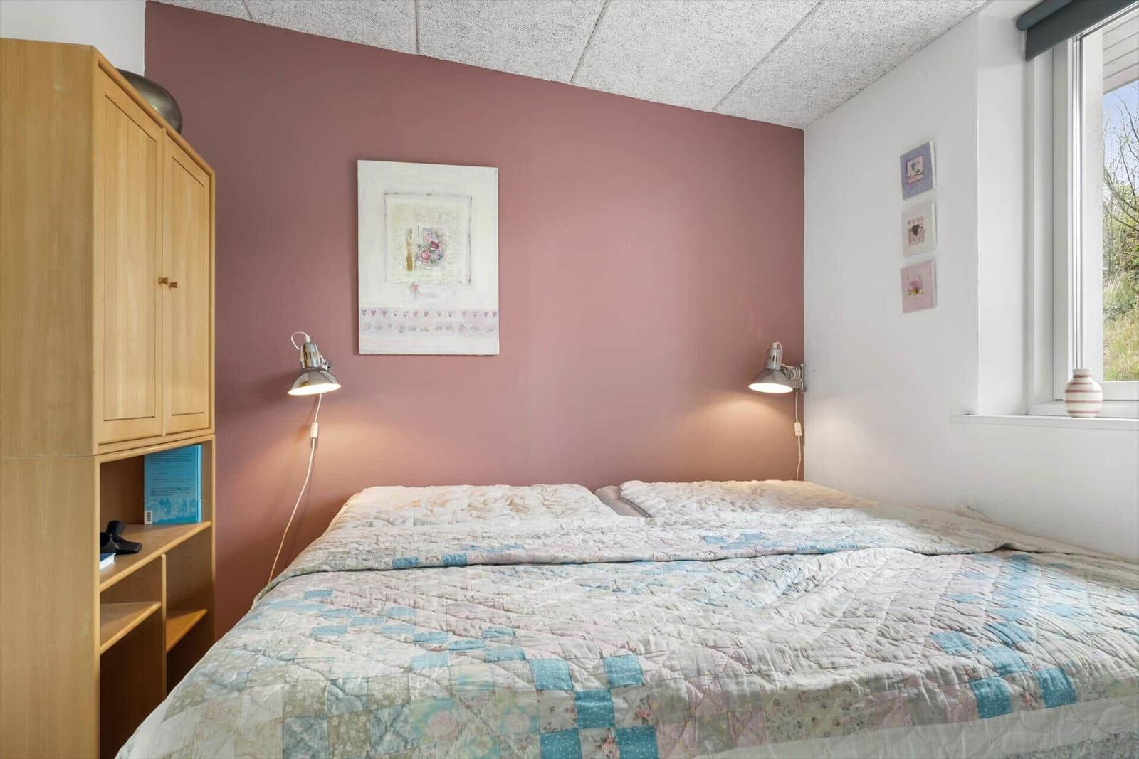 Bedroom with bed, wardrobe, and window. Wall color pink. Ceiling with lights.