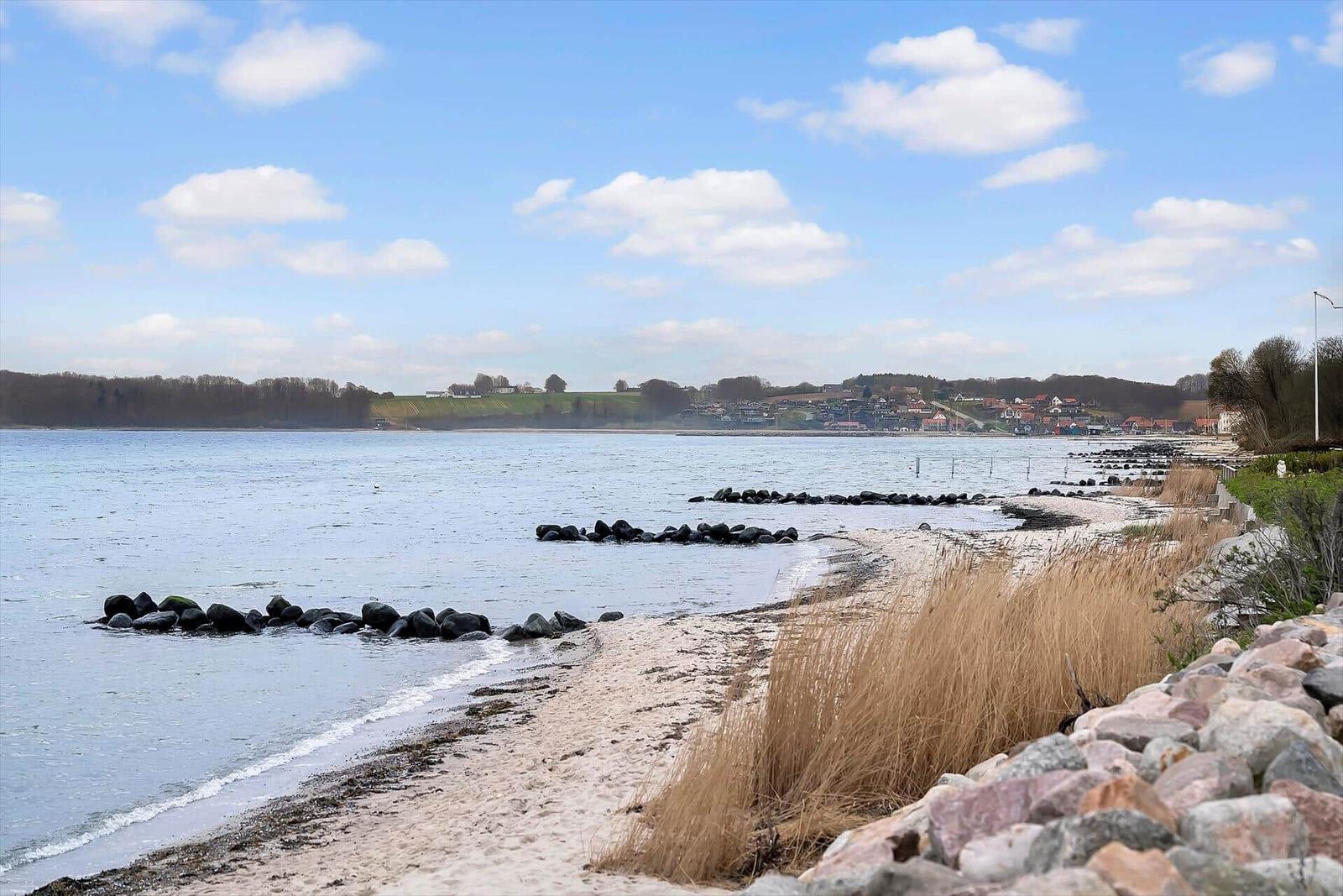 Beach with stones and grass, view of water and holiday home.