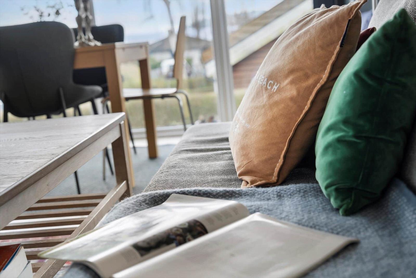 A sofa with cushions and a book. In the background, a table with chairs is visible.