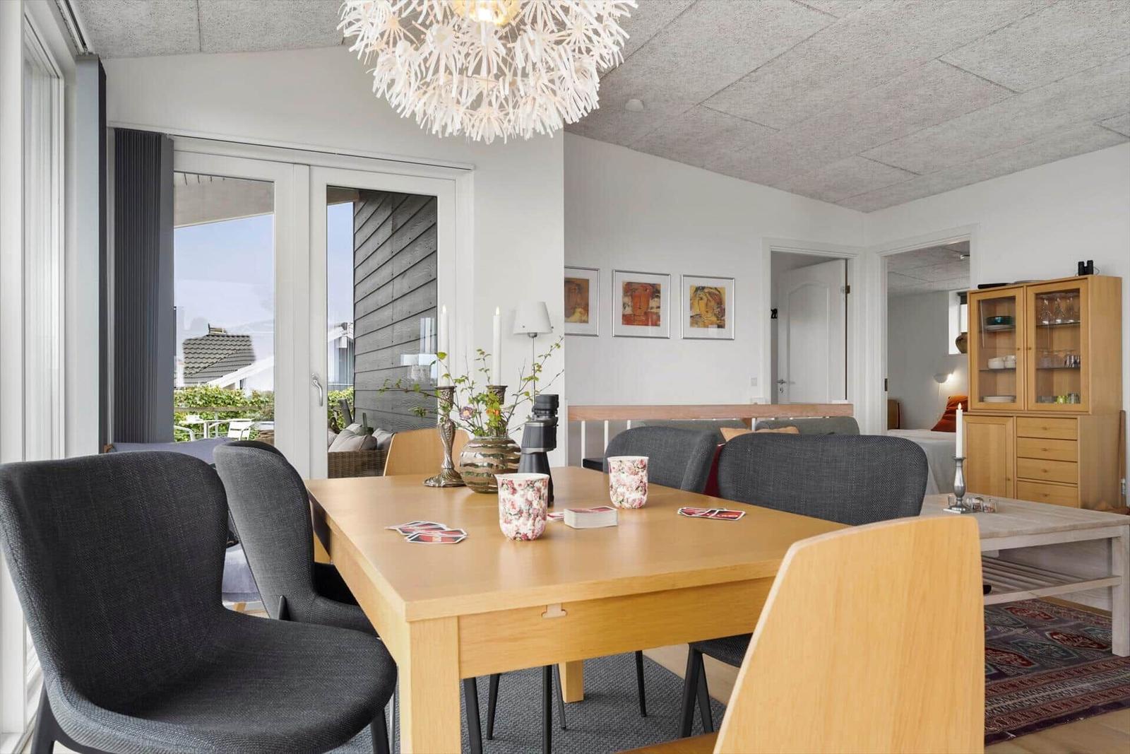 Dining room with wooden table, chairs, and ceiling light. Passage to living area and terrace.