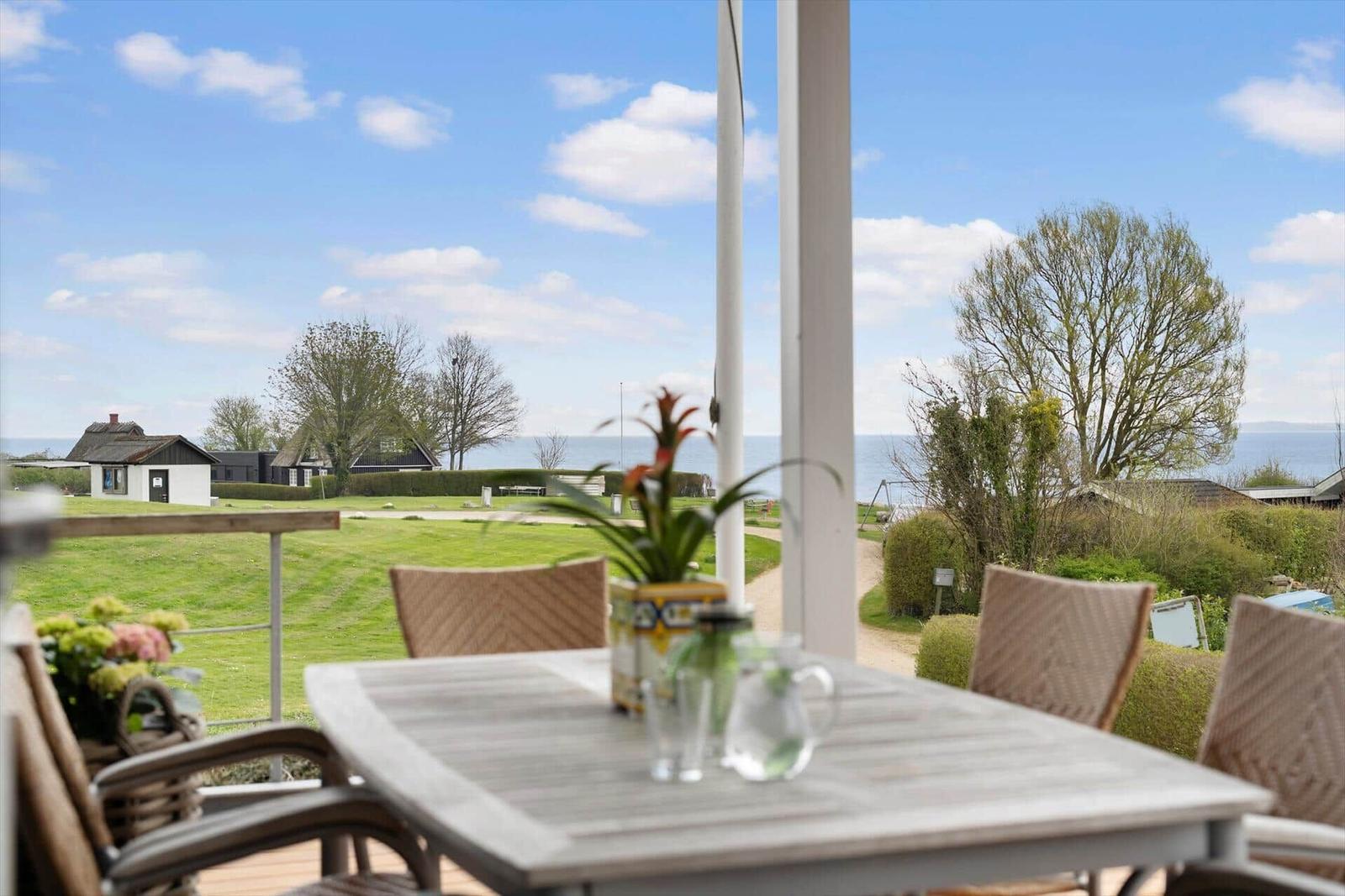 Terrace with table and chairs offers view of lawn and sea.