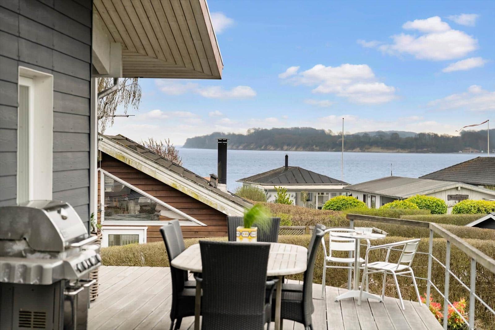 Deck with grill, table, and chairs. View of water and houses.