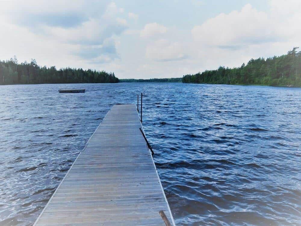 Holzsteg führt über das Wasser zu einem Boot. Wald umgibt den See.
