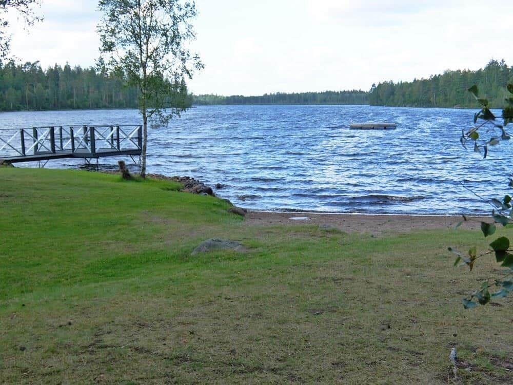 Seeufer mit Holzsteg und grünem Rasenbereich.