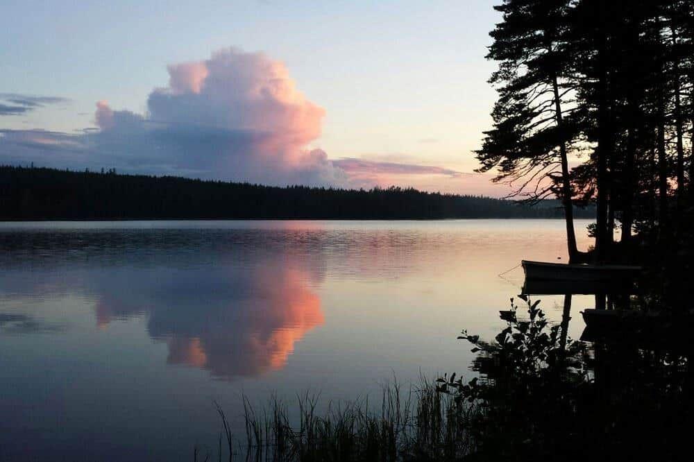 See bei Sonnenuntergang mit Boot und Bäumen