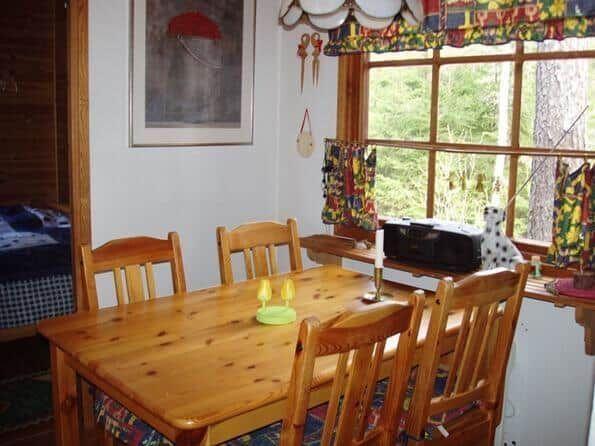 Holztisch mit Stühlen, Fenster mit bunten Vorhängen und Wandbild.