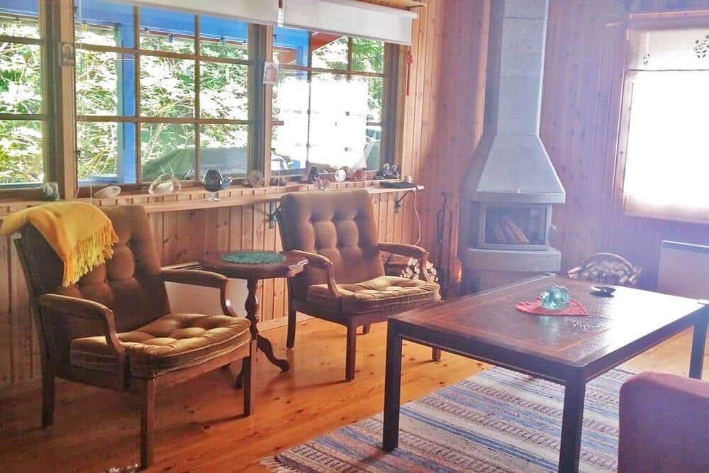 Wohnzimmer mit Holzwand, Kamin, zwei Sesseln und Holztisch.