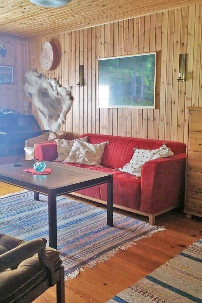 Ein Wohnzimmer mit rotem Sofa, Holzwand und Holzboden. Es gibt einen Tisch und einen Teppich.