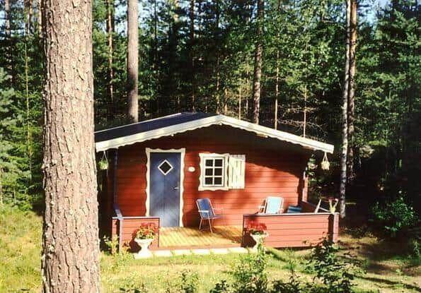 Rotes Holzhaus mit Veranda im Wald. Tür und Fenster sind sichtbar.