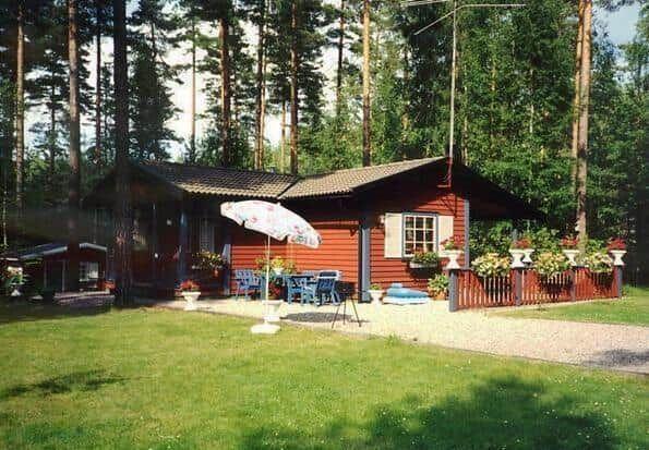 Rotes Holzhaus mit Garten, Terrasse und Sonnenschirm in Waldnähe.