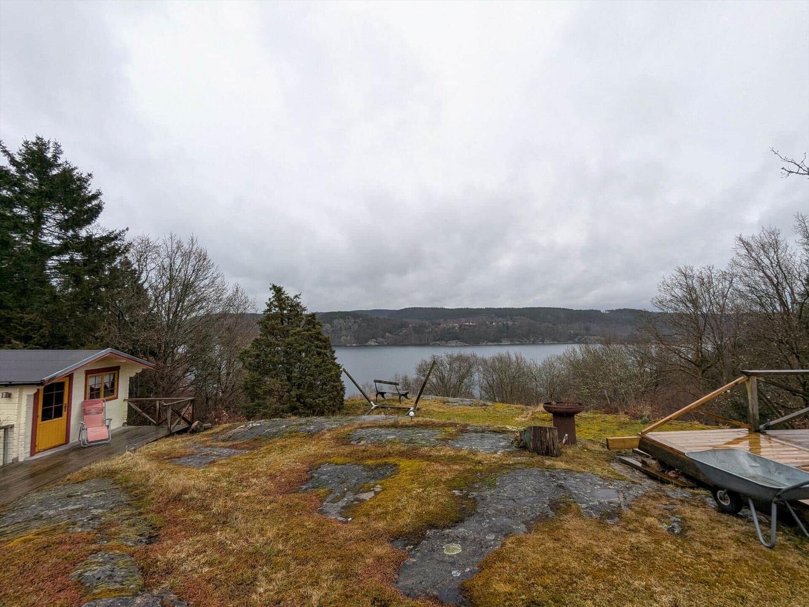 Haus mit Blick auf See, Holzterrasse und Grillplatz auf Steinflur.