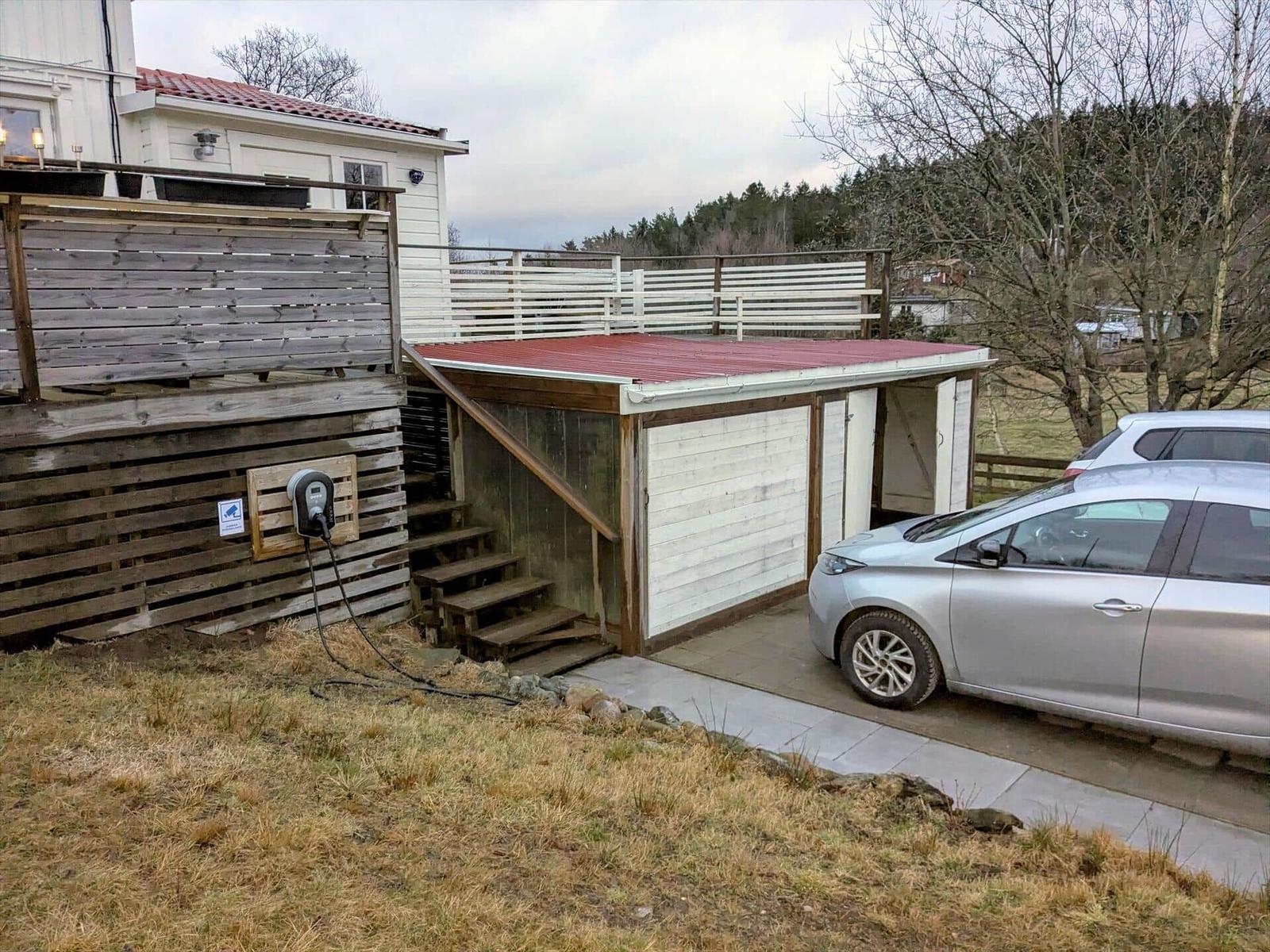 Hinterhof mit Carport, Ladestation und Holzterrasse. Ein Auto steht bereit.