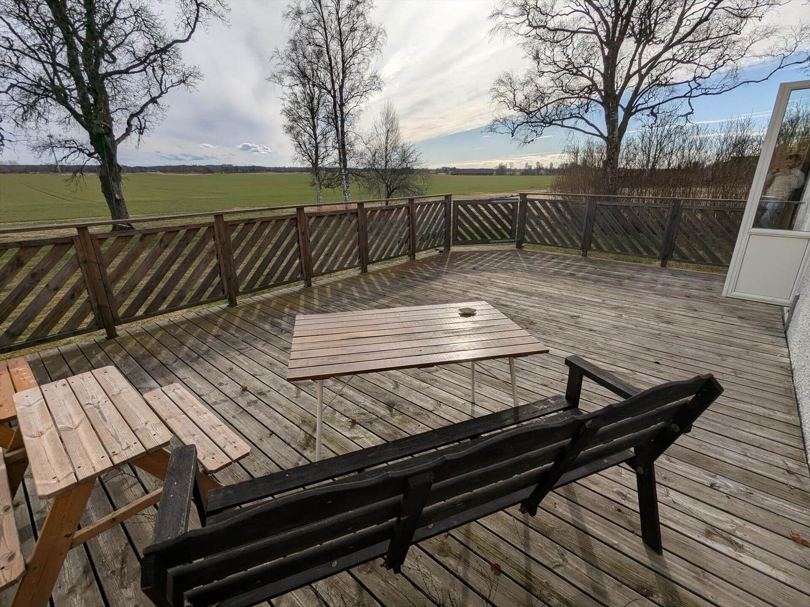 Holzterrasse mit Tisch und Bank, Blick auf Felder und Bäume.