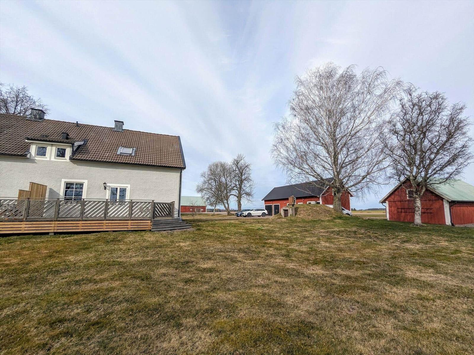 Haus mit Terrasse, rote Scheunen und Grünfläche im Freien.