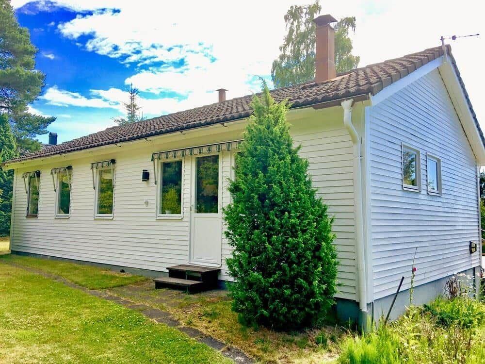 Weißes Haus mit braunem Dach und grüner Umgebung.