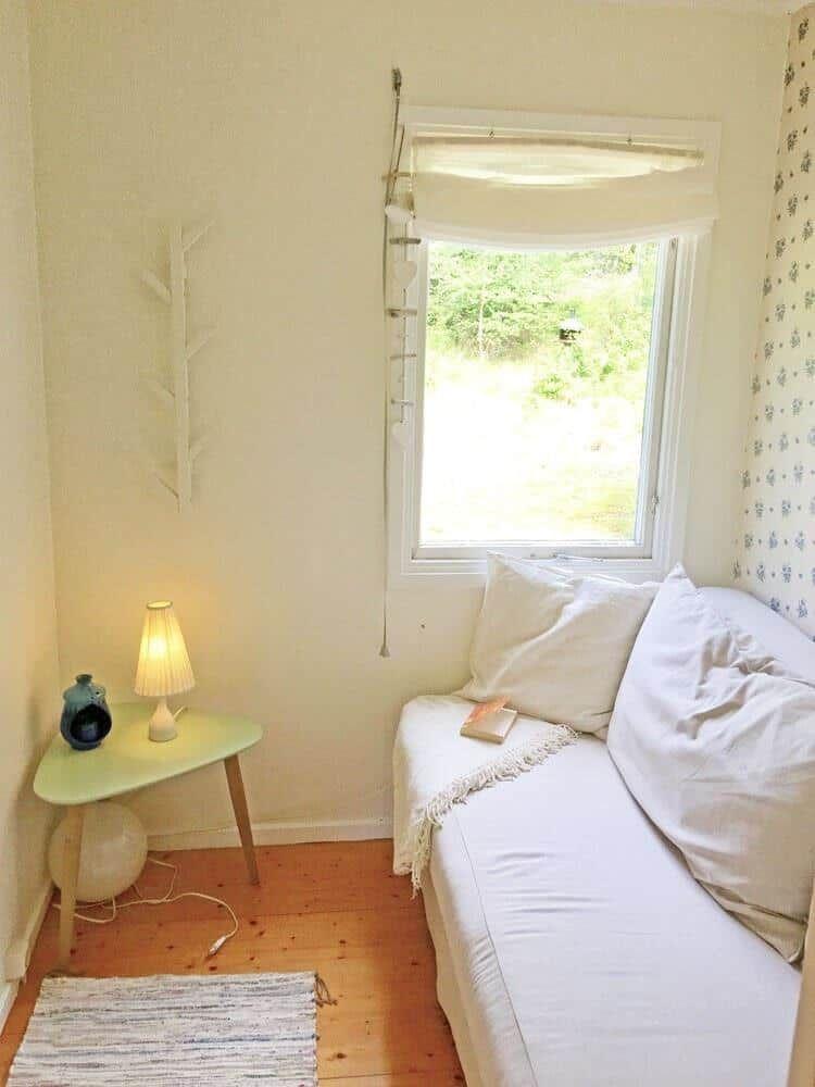 Ein Schlafzimmer mit weißem Bett, Fenster und Nachttisch mit Lampe.