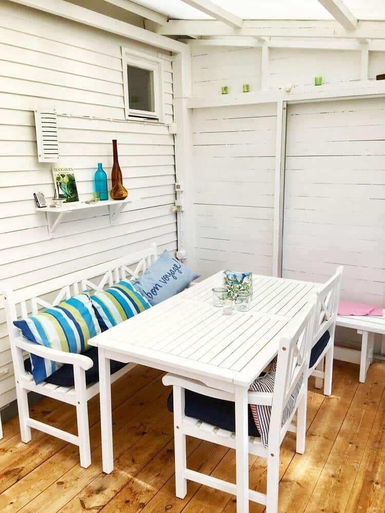 Weißer Holzterrasse mit Tisch, Stühlen und Kissen.