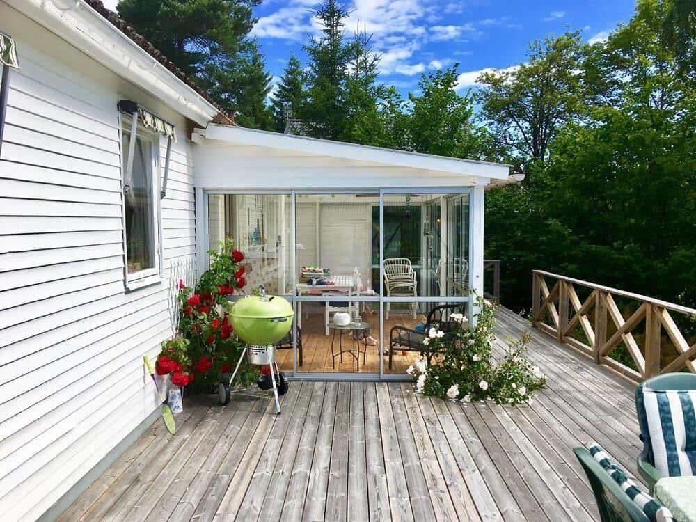 Terrasse mit Grill, Blumen und Glasveranda im Hintergrund.