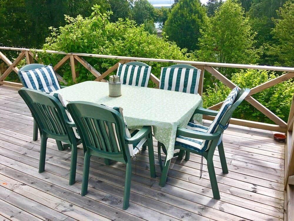 Terrasse mit Tisch und sechs Stühlen, umgeben von grüner Vegetation.