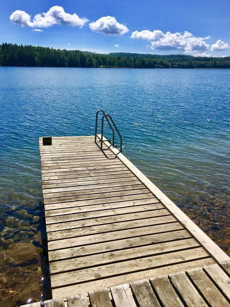 Holzsteg mit Leiter führt ins klare Wasser eines Sees.