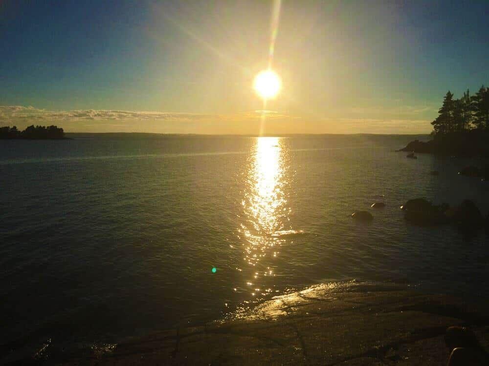 Sonnenuntergang über dem Wasser mit Felsen und Bäumen am Ufer.