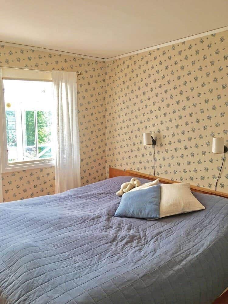 Schlafzimmer mit Bett, Fenster und Tapete mit Blumenmuster.