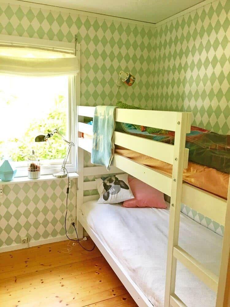 Zimmer mit Doppelstockbett, grün-weißem Tapetenmuster und Holzboden.