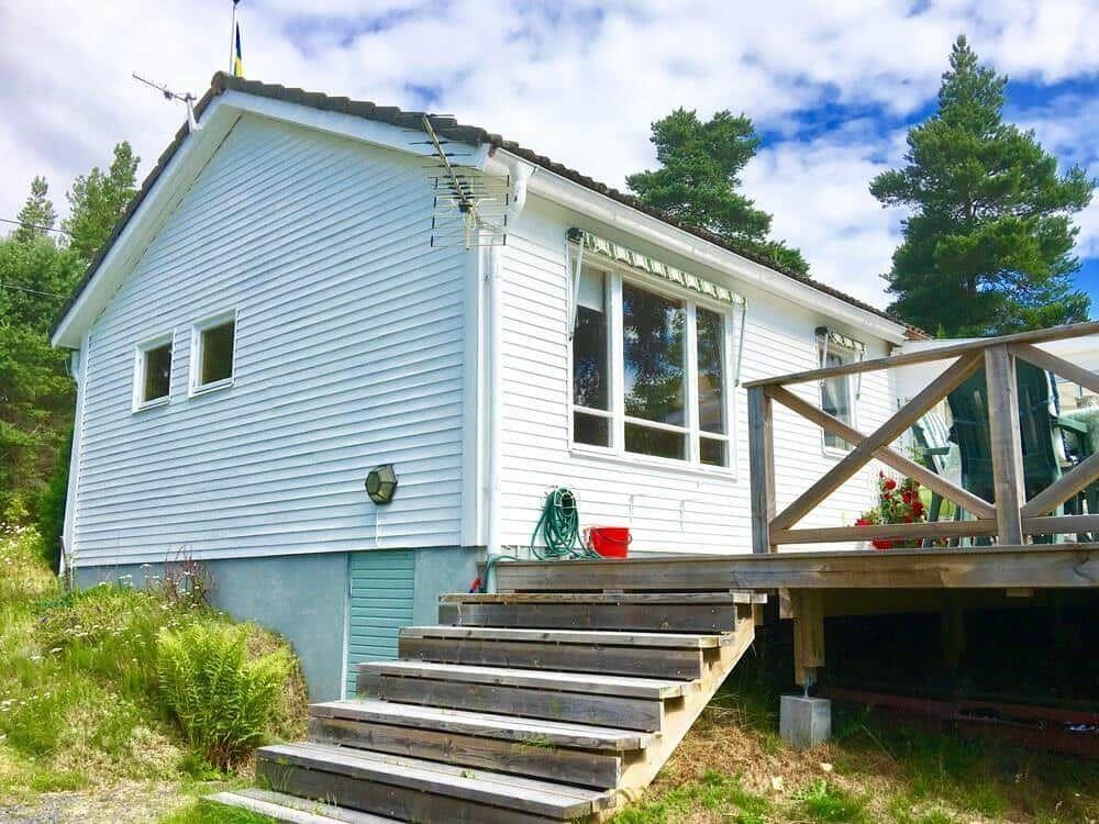 Wohnhaus mit Holzterrasse und Stufen. Umgeben von Bäumen und Grün.