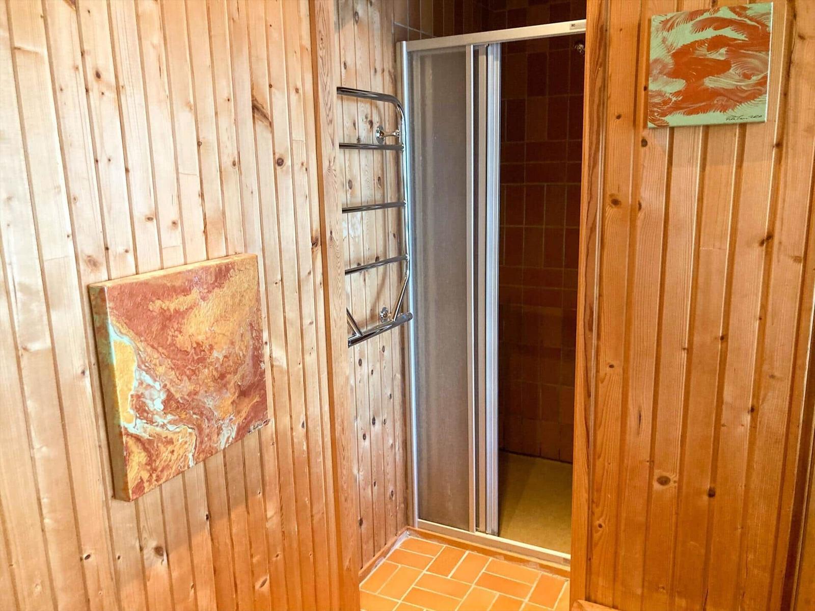 Duschkabine mit Glaswand, Holzwand und zwei Wandbildern.