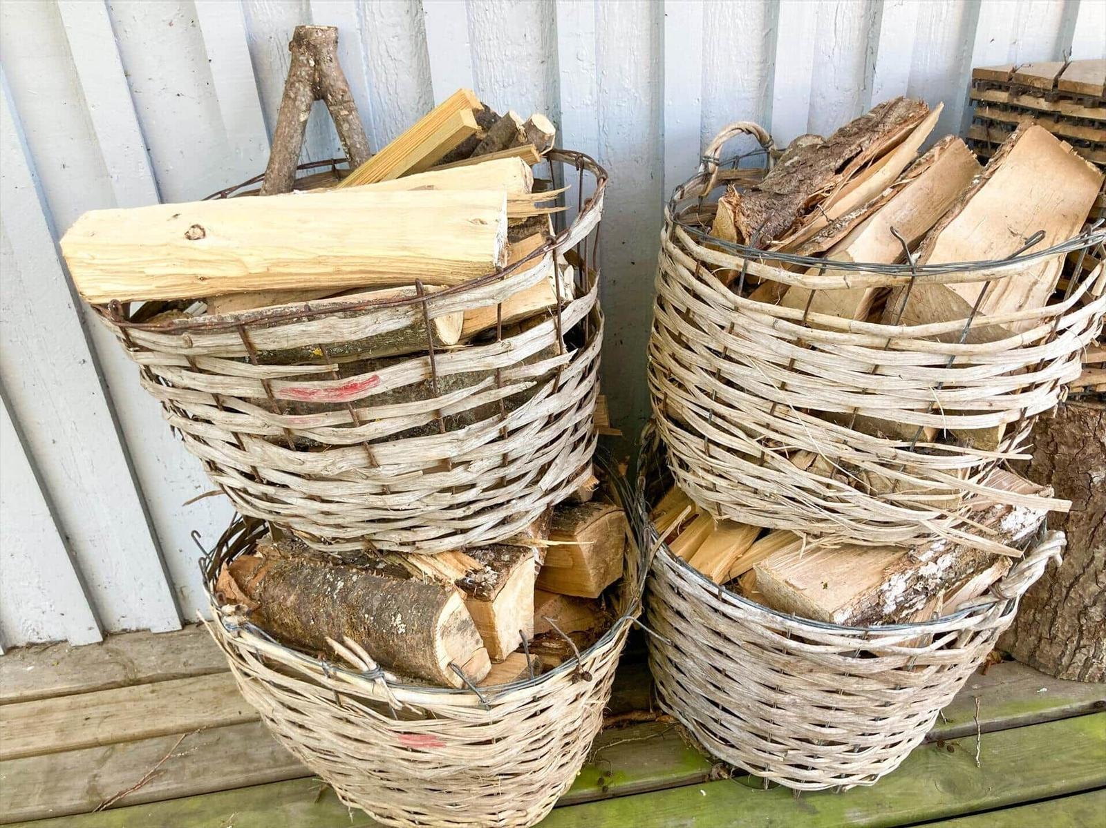 Zwei geflochtene Körbe mit Brennholz stehen auf einer Holzbank.