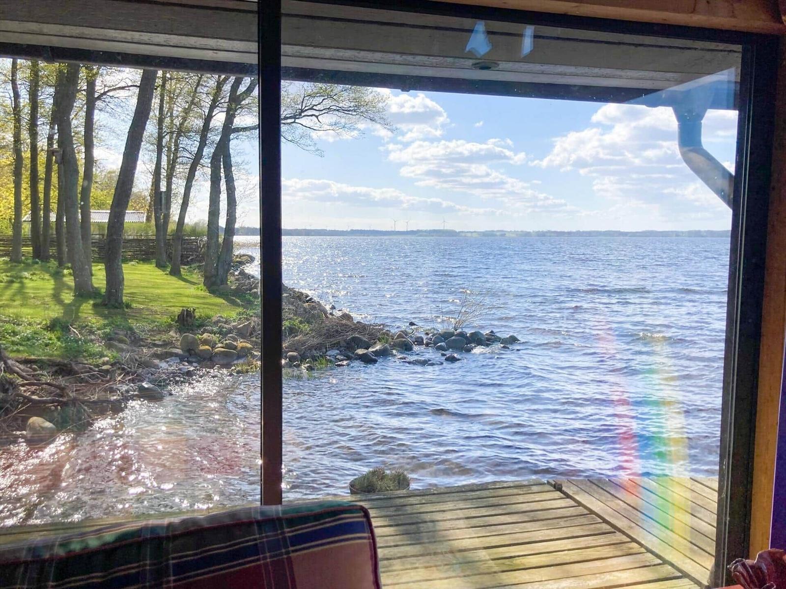 Blick auf See mit Steilufer und Bäumen durch großes Fenster