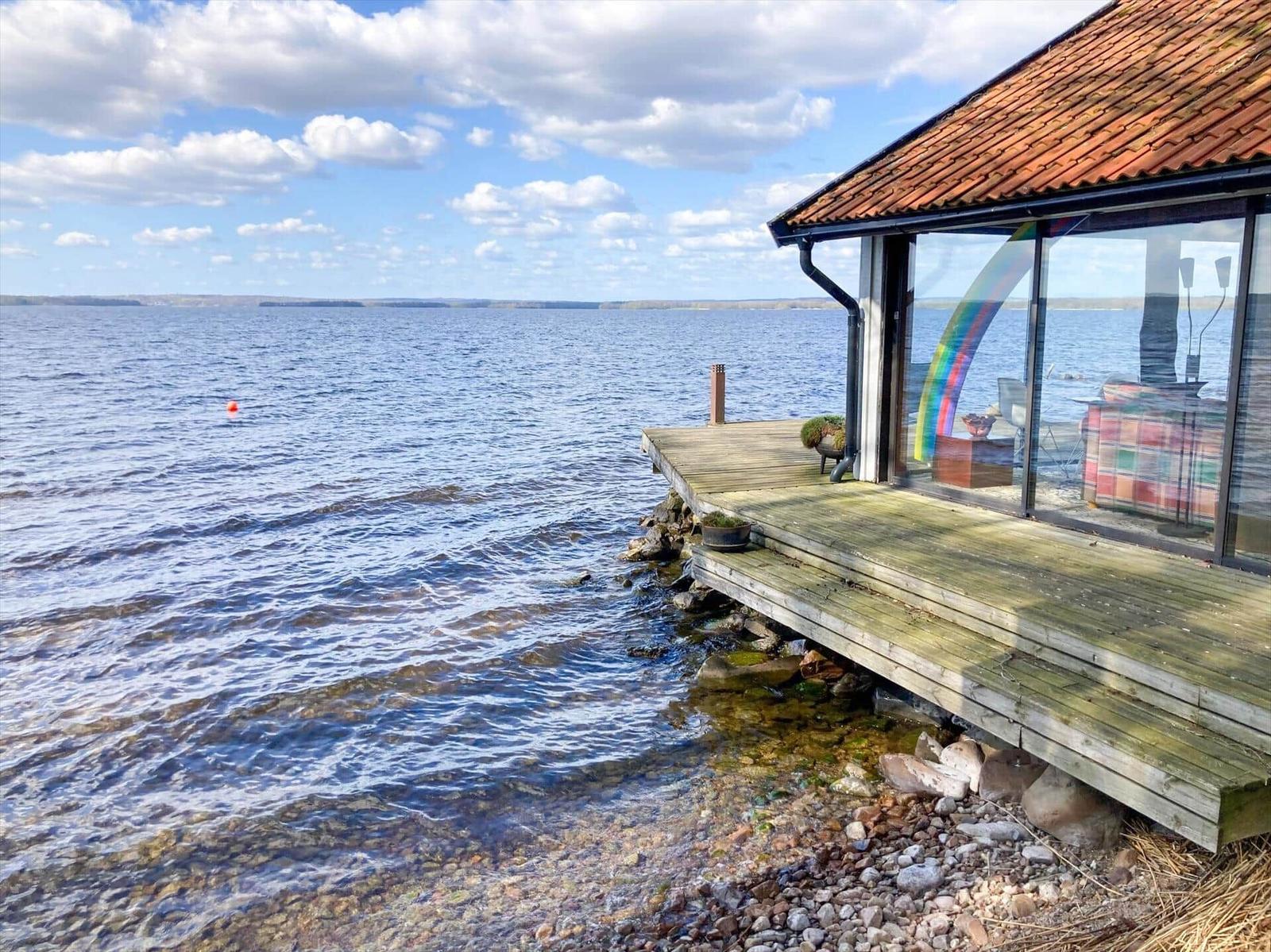 Haus mit Holzterrasse direkt am Wasser mit Blick auf See und Himmel.