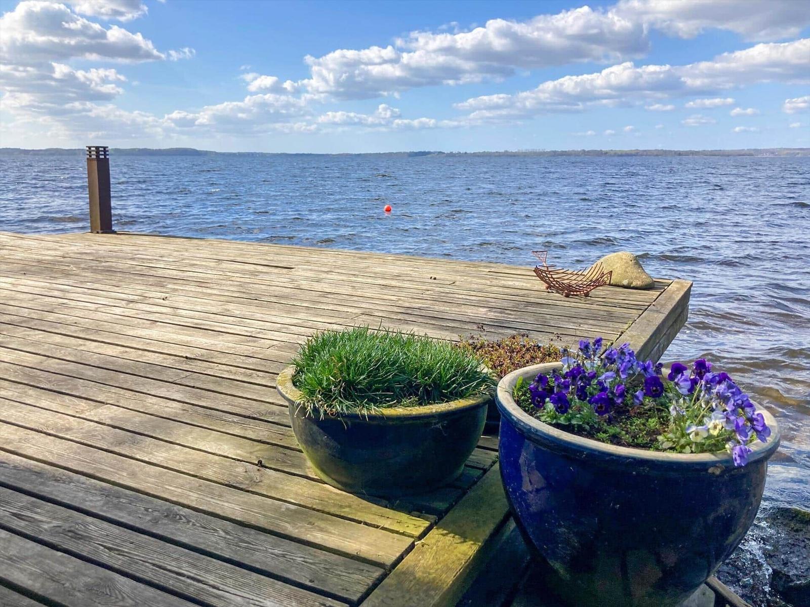 Holzterrasse am Wasser mit Blumenkästen und Blick auf See.