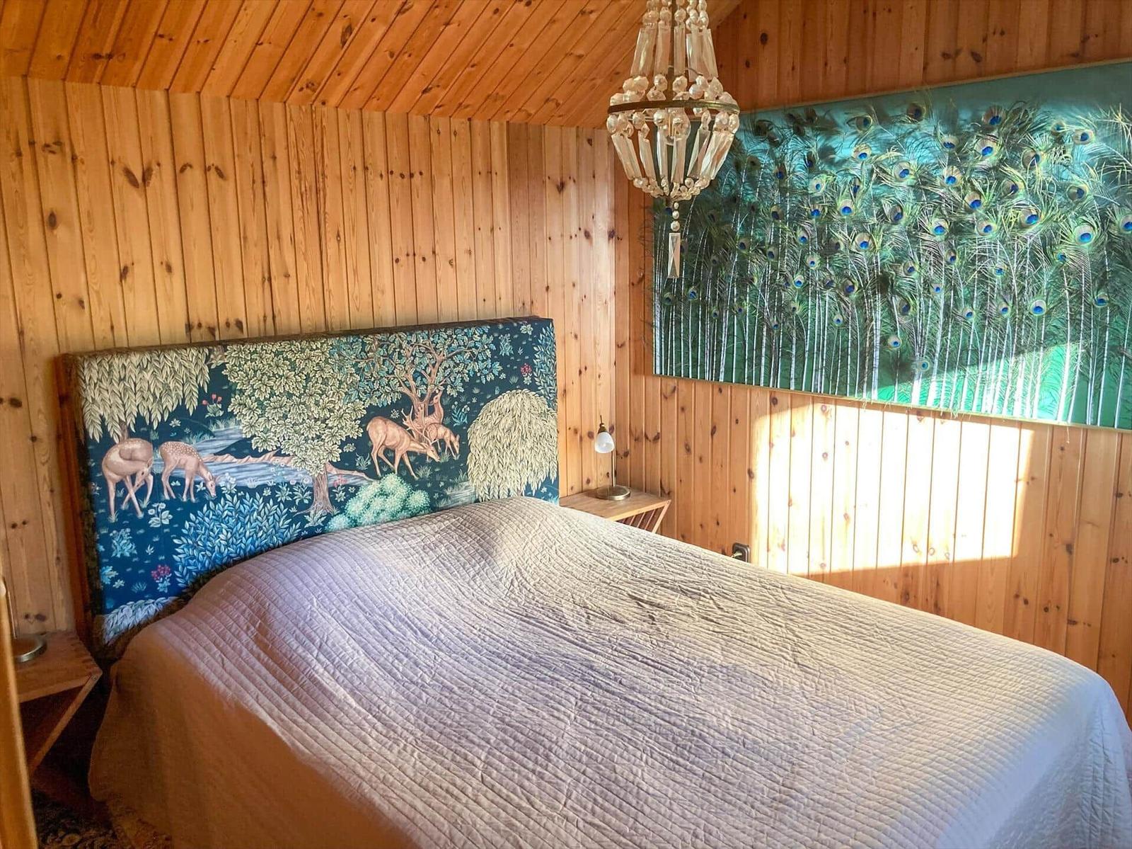 Schlafzimmer mit Holzwänden, Bett mit Tiermotivkopfteil und Wandbild mit Pfauenfedern.