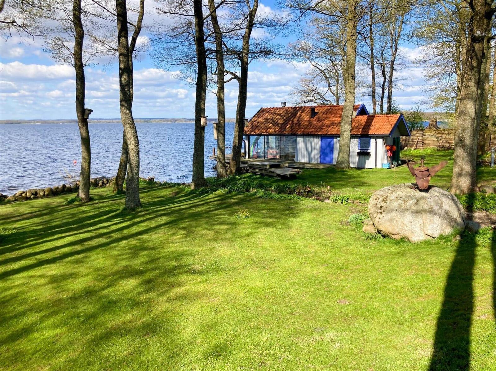 Haus mit Terrasse am See, umgeben von Bäumen und Gras.