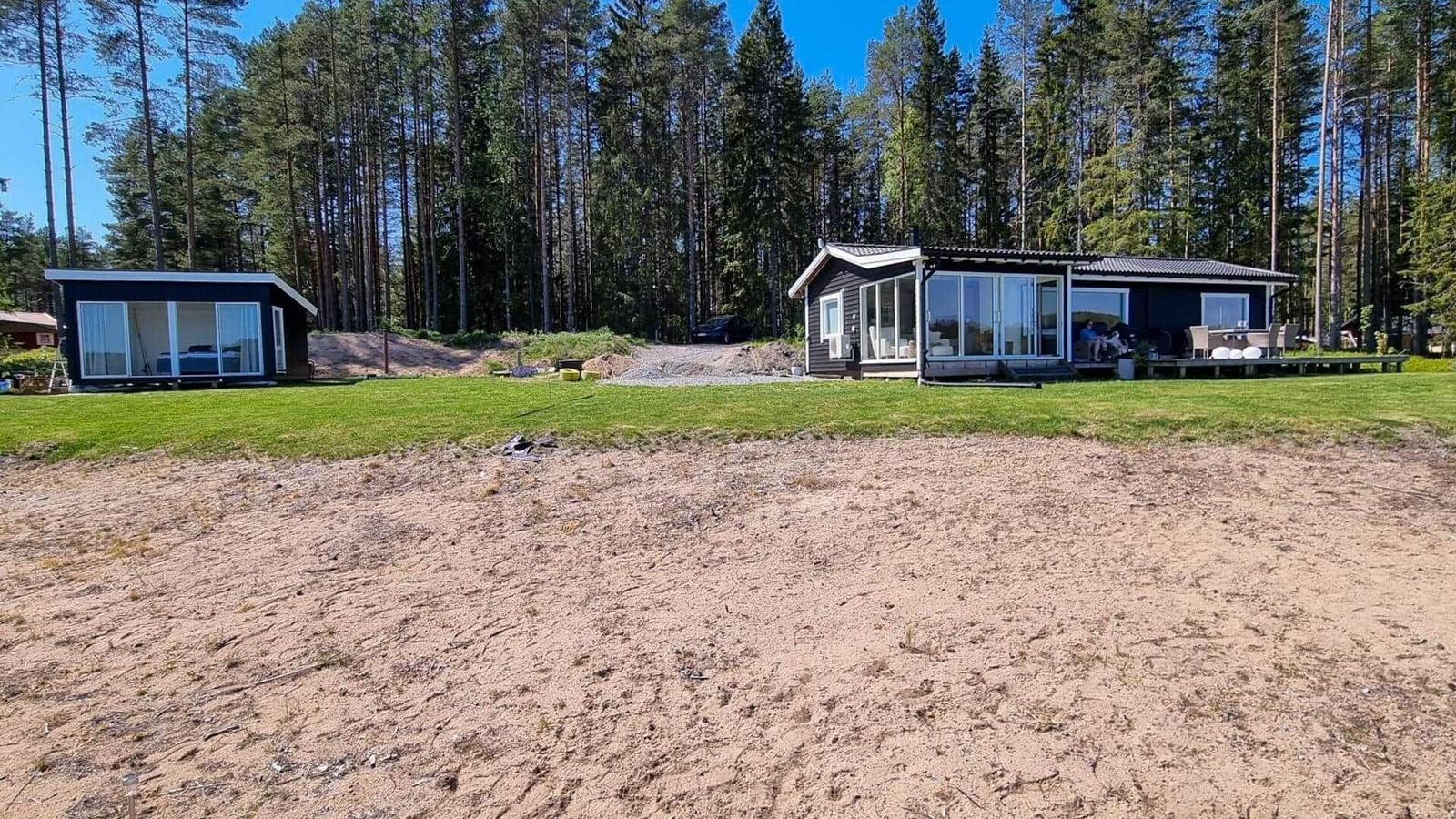 Zwei Häuser mit Terrassen stehen auf grünem Grundstück vor einem Wald.