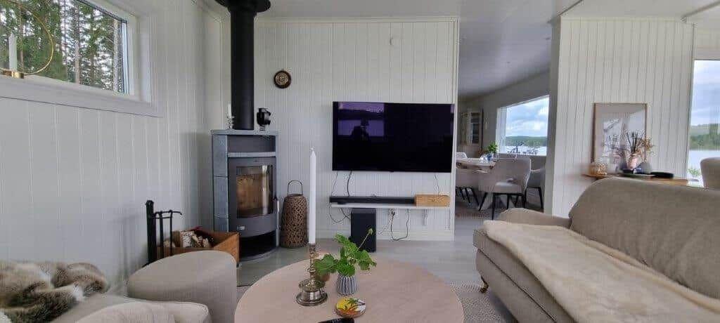 Wohnzimmer mit Kamin, Fernseher und Sofa. Durchgang zur Essnische mit Blick auf Wasser.