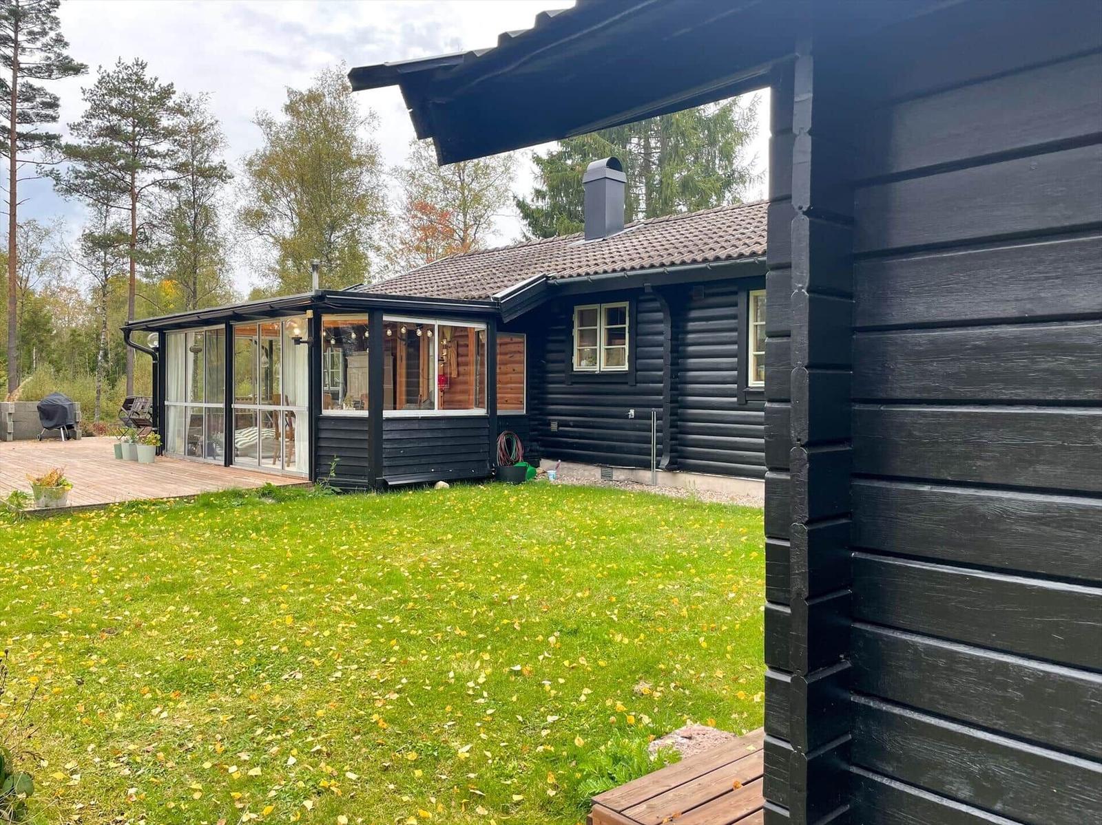 Schwarze Holzhütte mit Glasveranda und grünem Rasen im Wald