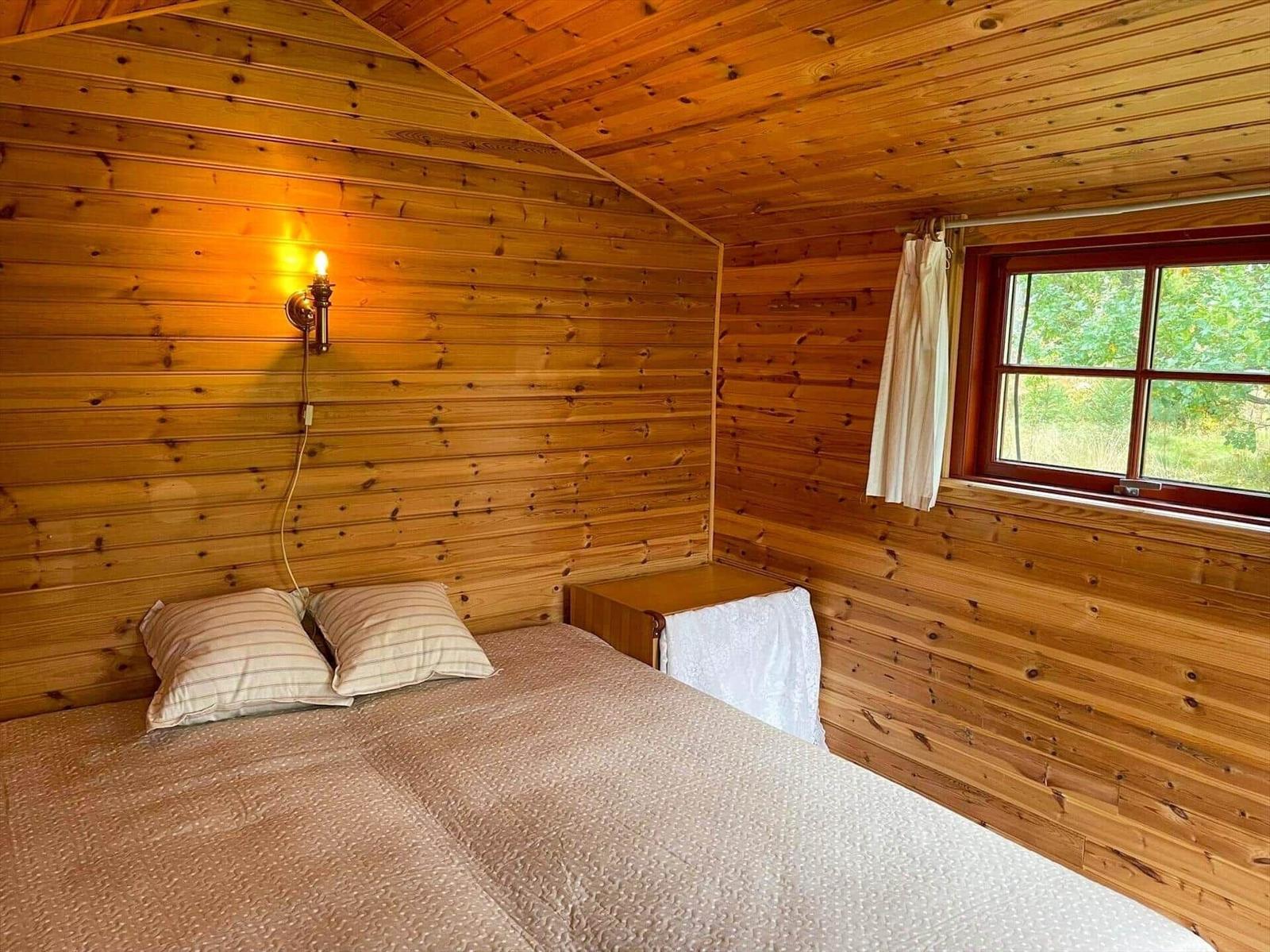 Schlafzimmer mit Holzwand, Bett und Fenster.