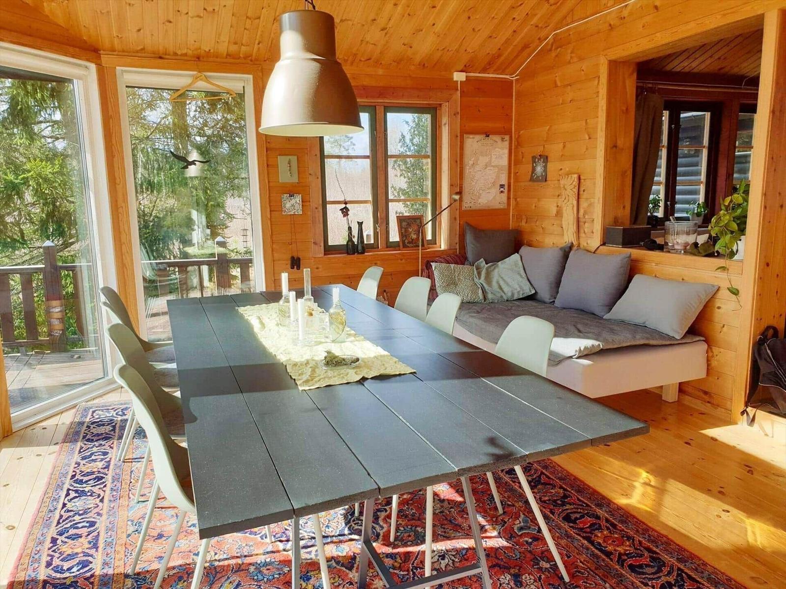 Esszimmer mit Holzwand, Tisch, Stühlen und Sofa. Durchgang zur Terrasse.